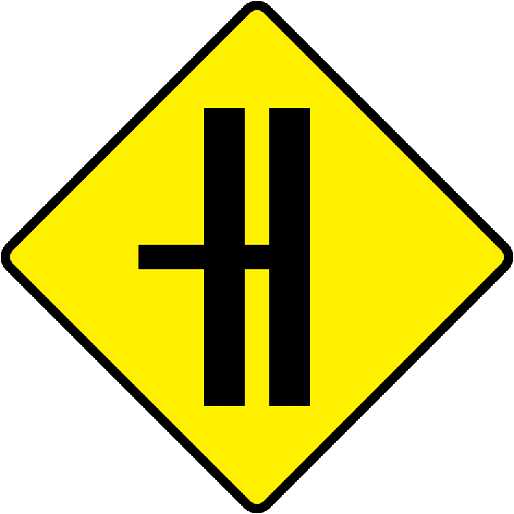 A triangular warning traffic sign in Ireland depicting side road on dual c'way - left (with cr break). Memorize for DTT.